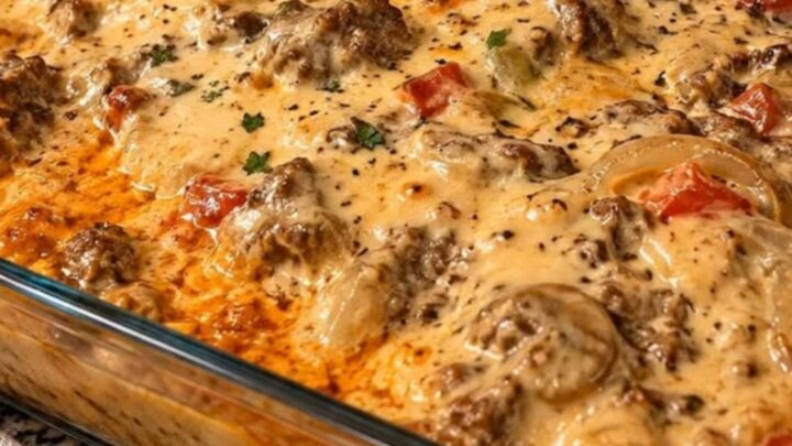 A close-up of a cheesy jerk chicken pasta bake in a glass dish with a serving spoon pulling out a portion.