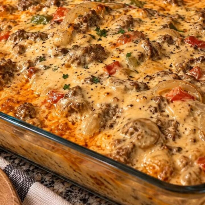A close-up of a cheesy jerk chicken pasta bake in a glass dish with a serving spoon pulling out a portion.