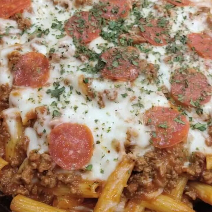 A steaming cast-iron skillet filled with Cheesy Pizza Hamburger Helper topped with pepperoni.