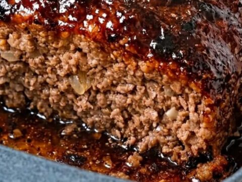 A thick, juicy slice of meatloaf with a shiny, sticky glaze served in a blue ceramic dish.
