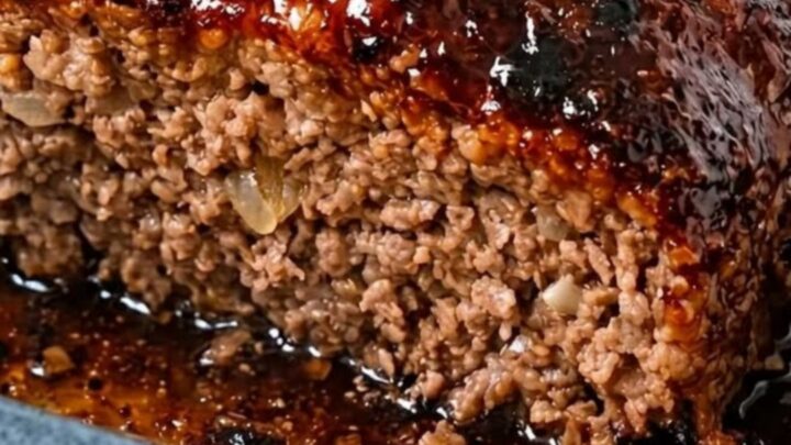 A thick, juicy slice of meatloaf with a shiny, sticky glaze served in a blue ceramic dish.