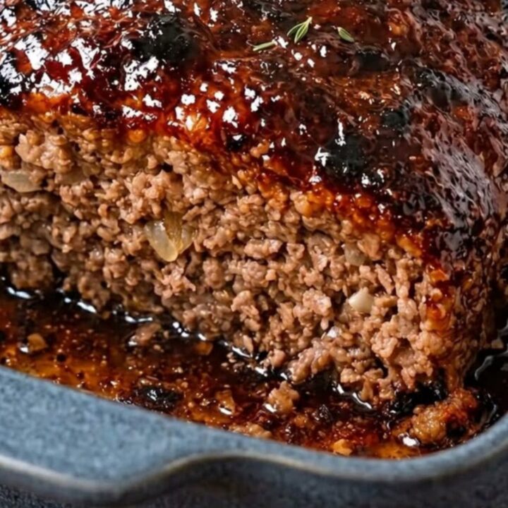 A thick, juicy slice of meatloaf with a shiny, sticky glaze served in a blue ceramic dish.