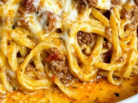 A close-up of a white bowl filled with creamy garlic cheddar beef spaghetti with a visible cheese pull.
