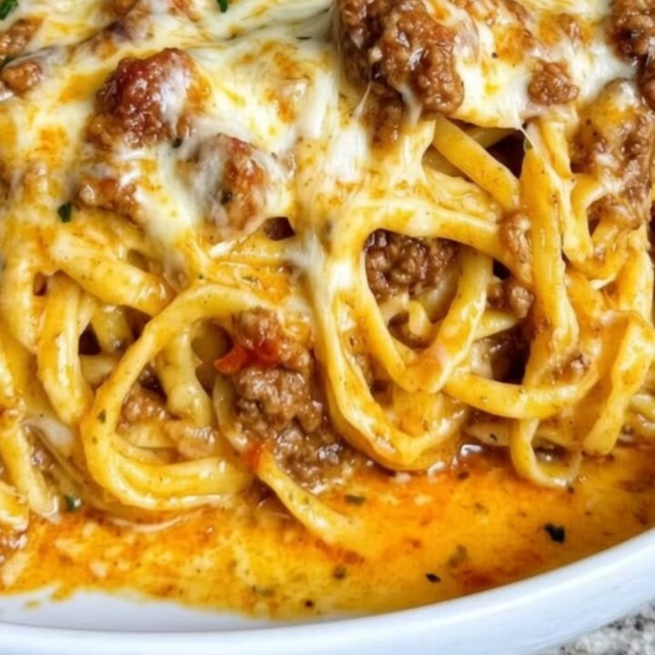 A close-up of a white bowl filled with creamy garlic cheddar beef spaghetti with a visible cheese pull.