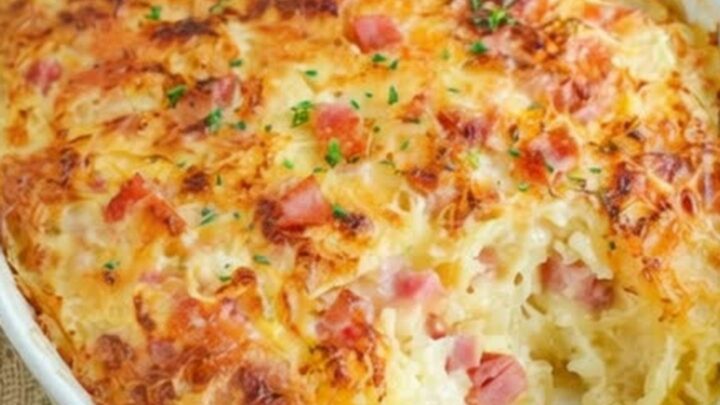 A golden-baked ham and cheese hash brown casserole in a white oval dish, showing melted cheese.