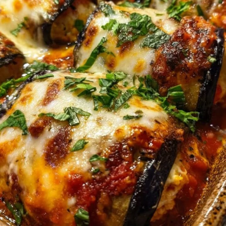 A close-up of cheesy stuffed eggplant rolls in a speckled baking dish, showing melted mozzarella and marinara.
