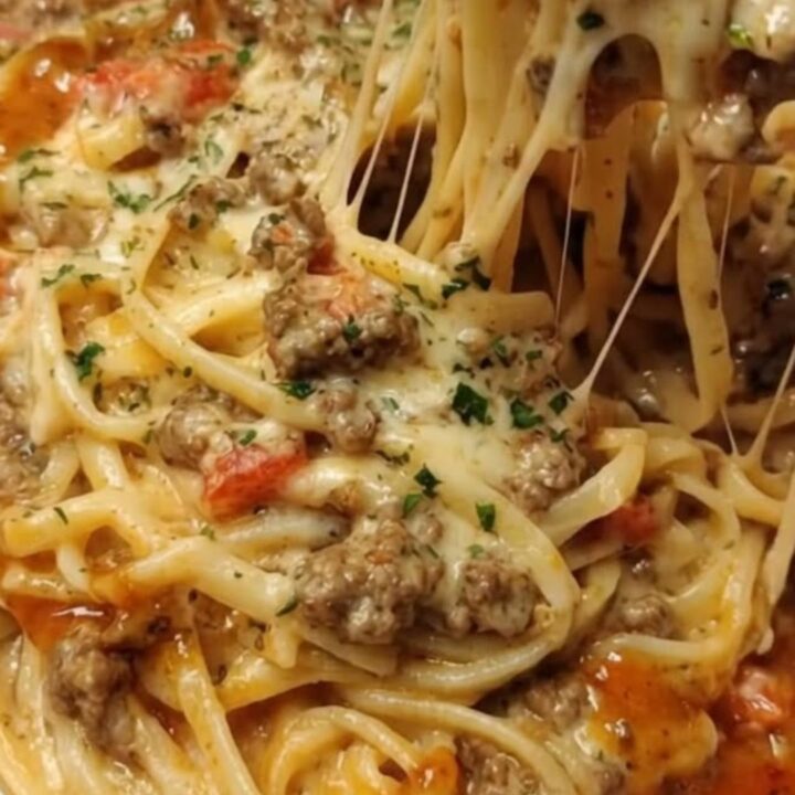 A steaming portion of creamy garlic butter beef linguine with a visible cheese pull on a white plate.