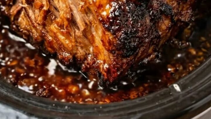 A succulent, shredded pork roast covered in a rich, dark honey garlic glaze inside a slow cooker.