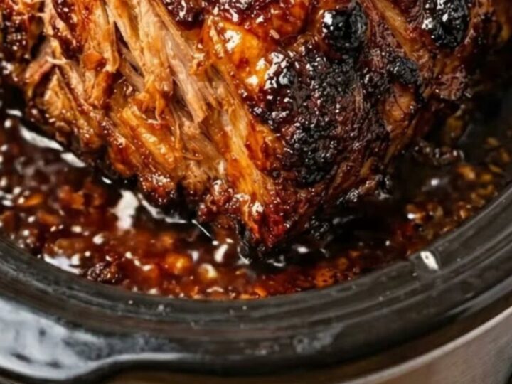 A succulent, shredded pork roast covered in a rich, dark honey garlic glaze inside a slow cooker.
