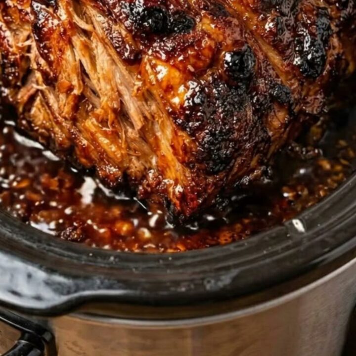 A succulent, shredded pork roast covered in a rich, dark honey garlic glaze inside a slow cooker.