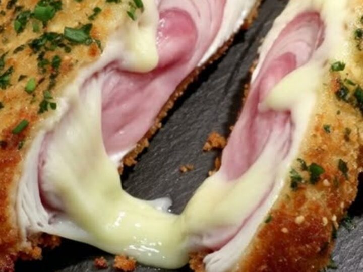 A golden-brown, crispy chicken cordon bleu on a dark slate platter, garnished with fresh green parsley.