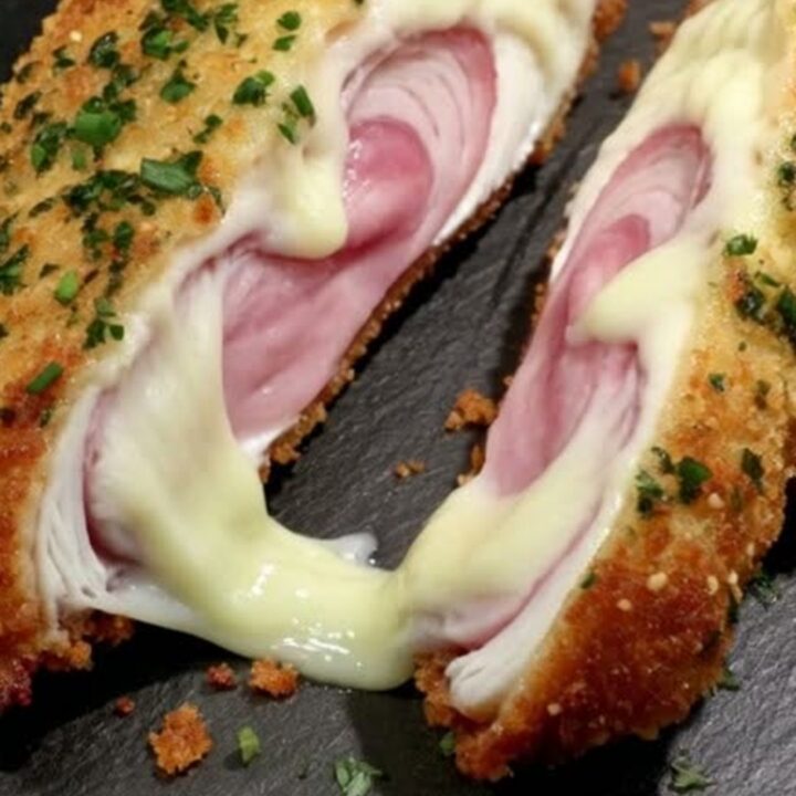 A golden-brown, crispy chicken cordon bleu on a dark slate platter, garnished with fresh green parsley.