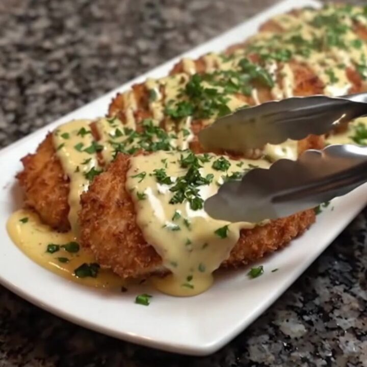 Golden-brown crispy chicken cutlets topped with a creamy garlic herb sauce on a white platter.