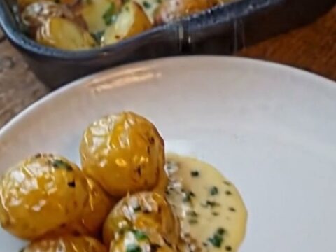 A thick, juicy slice of beef roast topped with a glossy garlic herb cream sauce next to roasted baby potatoes in a cast-iron