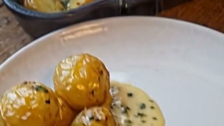 A thick, juicy slice of beef roast topped with a glossy garlic herb cream sauce next to roasted baby potatoes in a cast-iron