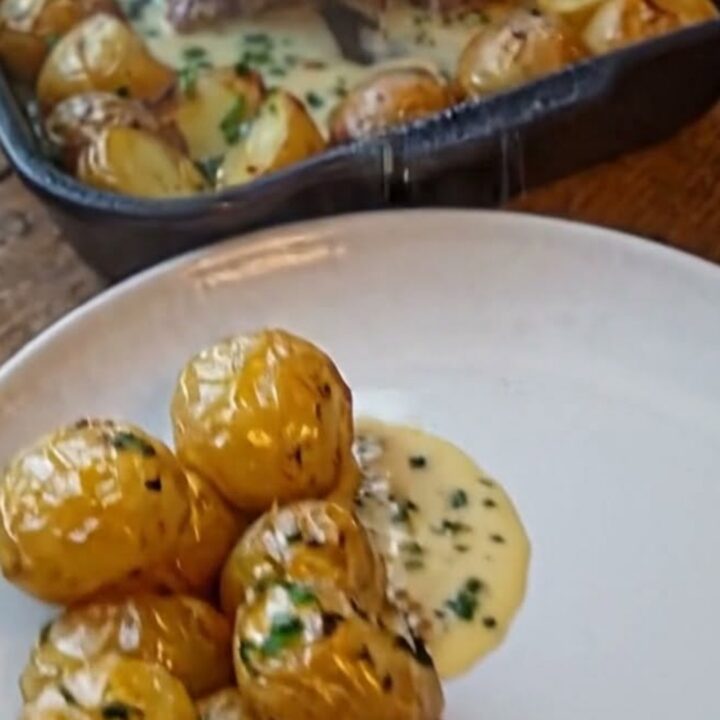 A thick, juicy slice of beef roast topped with a glossy garlic herb cream sauce next to roasted baby potatoes in a cast-iron