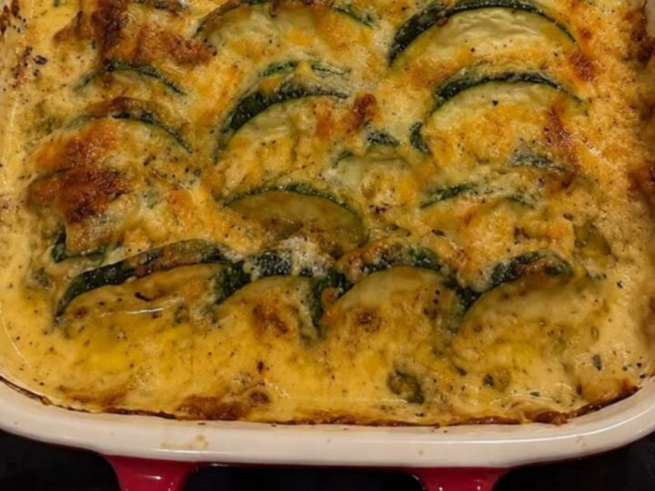 A steaming portion of cheesy zucchini and ground beef casserole being lifted from a baking dish with a spatula.