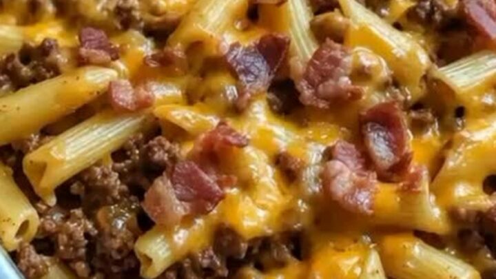 A steaming, cheesy bacon cheeseburger pasta bake in a baking dish with a spatula lifting a portion.