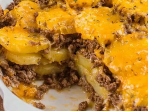 A steaming cheesy ground beef and potato casserole served in a white oval baking dish.