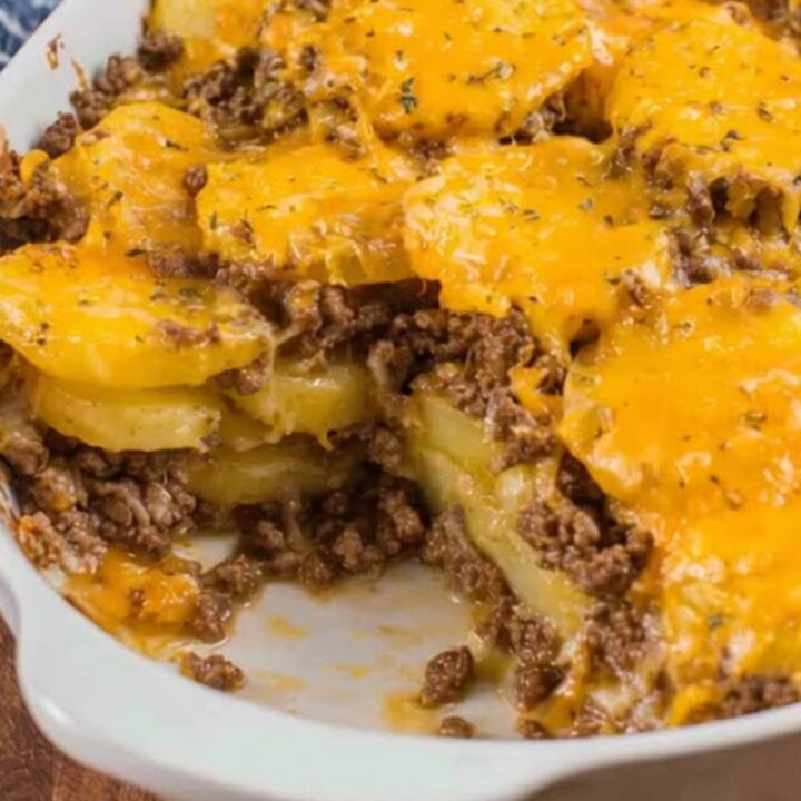 A steaming cheesy ground beef and potato casserole served in a white oval baking dish.