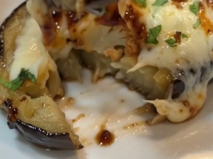 A warm baking dish filled with roasted eggplant halves topped with bubbling melted mozzarella and fresh parsley.