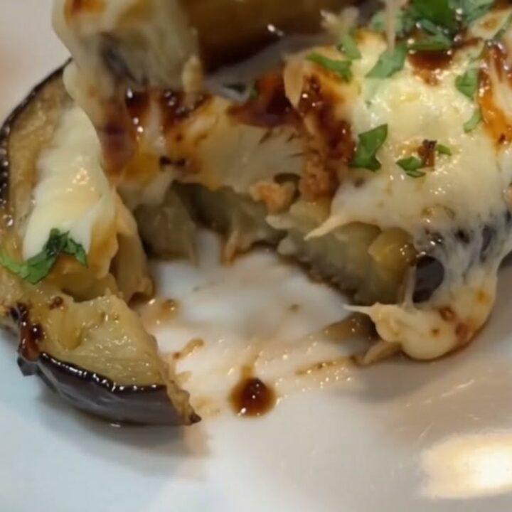 A warm baking dish filled with roasted eggplant halves topped with bubbling melted mozzarella and fresh parsley.