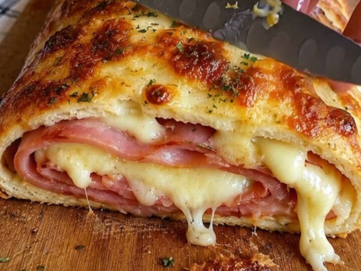 A golden-brown baked ham and cheese stromboli resting on a wooden cutting board.