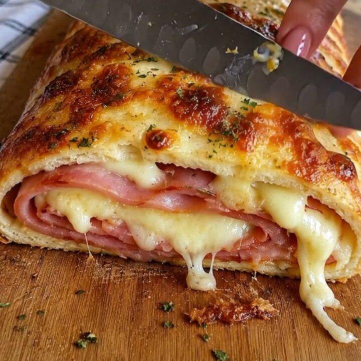 A golden-brown baked ham and cheese stromboli resting on a wooden cutting board.