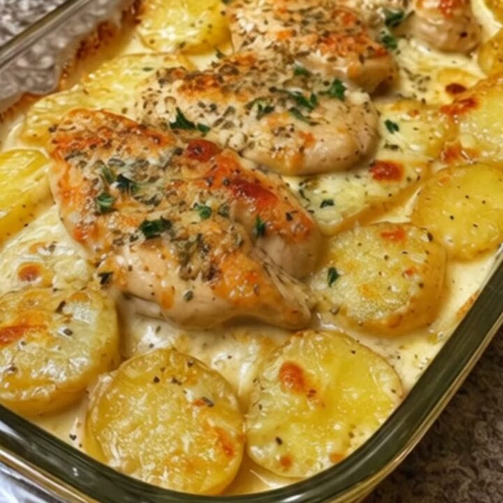 A clear glass baking dish filled with creamy chicken and golden potato coins, bubbling in a rich, cheesy sauce.
