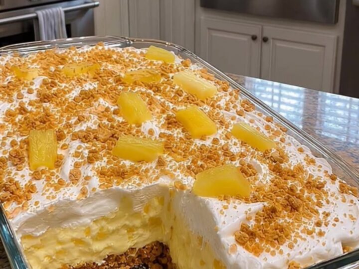 A metal spatula lifting a square of pineapple cream dessert from a 9x13 dish, showing distinct layers.