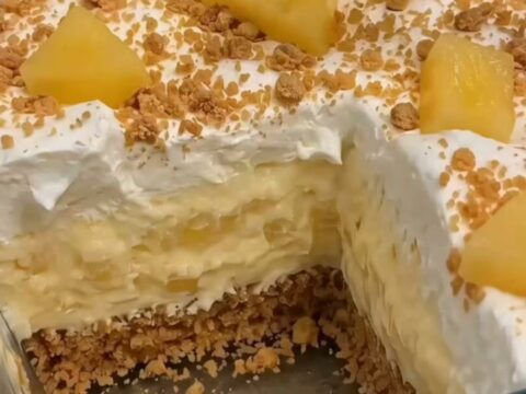 A chilled pineapple cream dessert in a glass dish with distinct layers of graham crust and creamy pineapple filling.