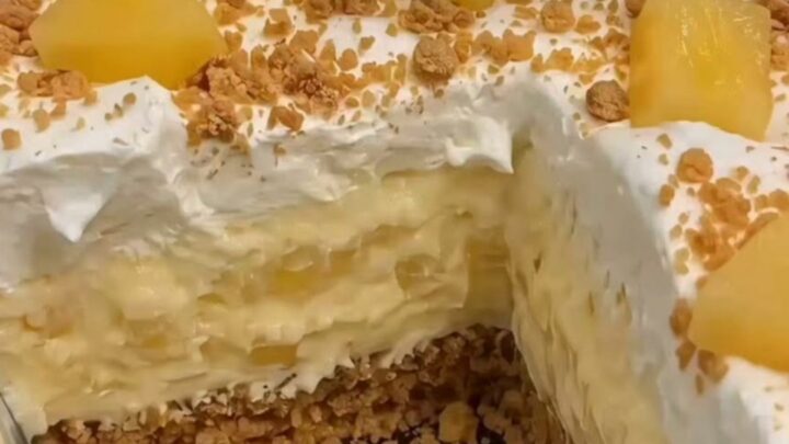 A chilled pineapple cream dessert in a glass dish with distinct layers of graham crust and creamy pineapple filling.