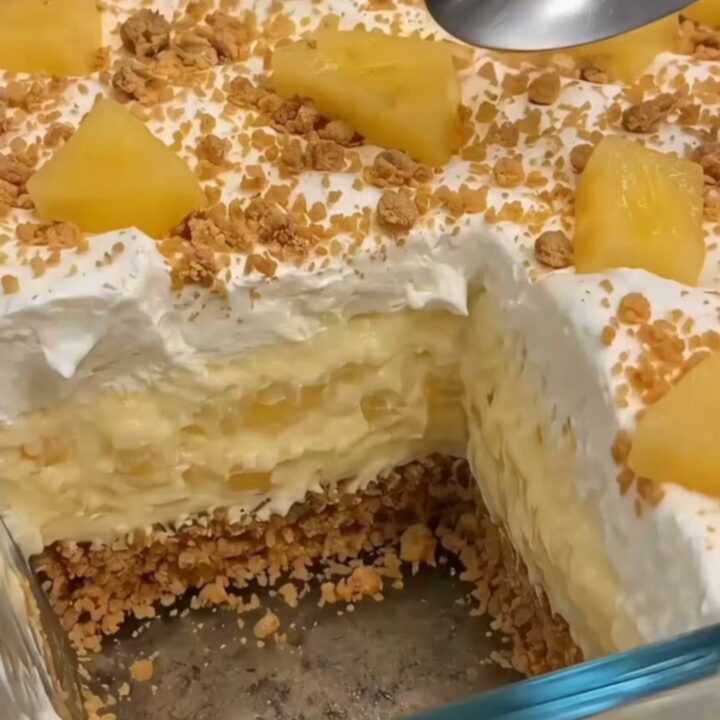 A chilled pineapple cream dessert in a glass dish with distinct layers of graham crust and creamy pineapple filling.