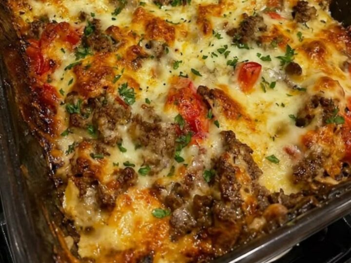 A steaming Philly cheesesteak casserole in a glass dish with melted cheese on top.