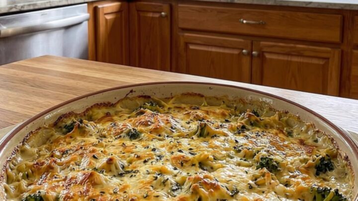 A golden-baked creamy chicken and broccoli orzo casserole in a round ceramic dish.