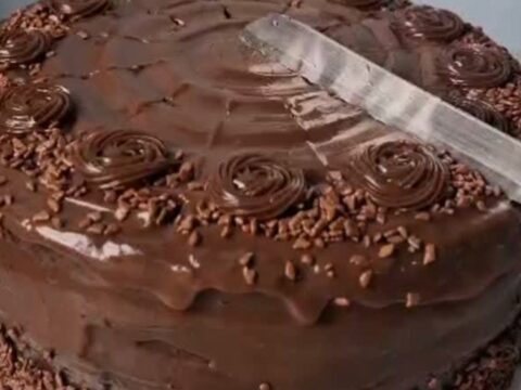 A slice of rich, dark chocolate fudge cake with glossy frosting on a white plate.