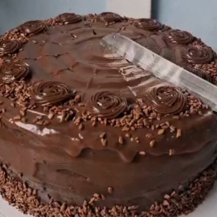 A slice of rich, dark chocolate fudge cake with glossy frosting on a white plate.