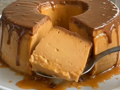 A glossy chocolate pudding ring drizzled with golden caramel sauce on a white plate.