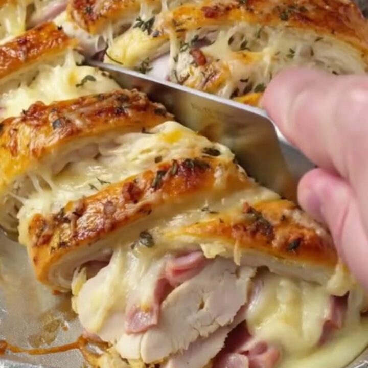 A golden-brown chicken ham and Swiss crescent braid sliced on a foil-lined baking sheet with melted cheese oozing out.