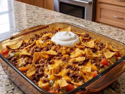 A steaming portion of walking taco bake being lifted from an amber glass dish, showcasing melted cheese and crunchy chips.