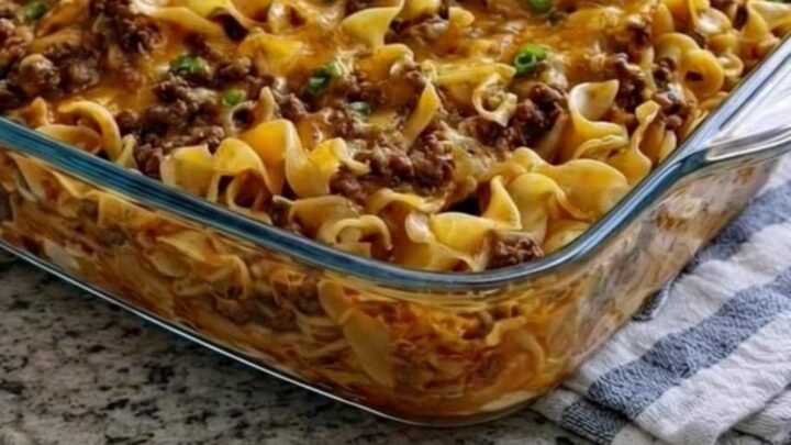 A cheesy beef and noodle casserole in a glass dish with a spatula lifting a portion.