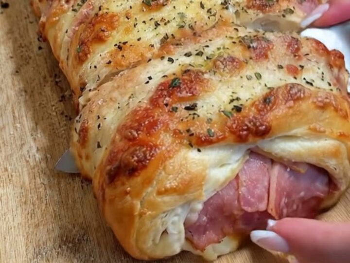 A golden-brown baked ham and cheese stromboli resting on a rustic wooden cutting board.