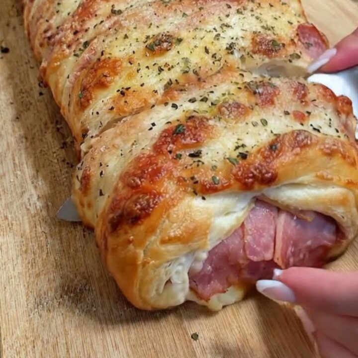 A golden-brown baked ham and cheese stromboli resting on a rustic wooden cutting board.