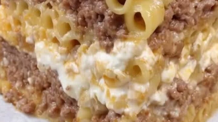 A tall slice of Greek pastitsio on a patterned plate, showing layers of tubular pasta, spiced beef, and golden béchamel.