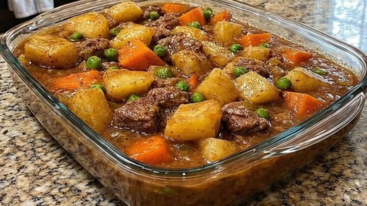 A steaming portion of beef stew casserole in a white bowl with chunks of beef and potatoes.