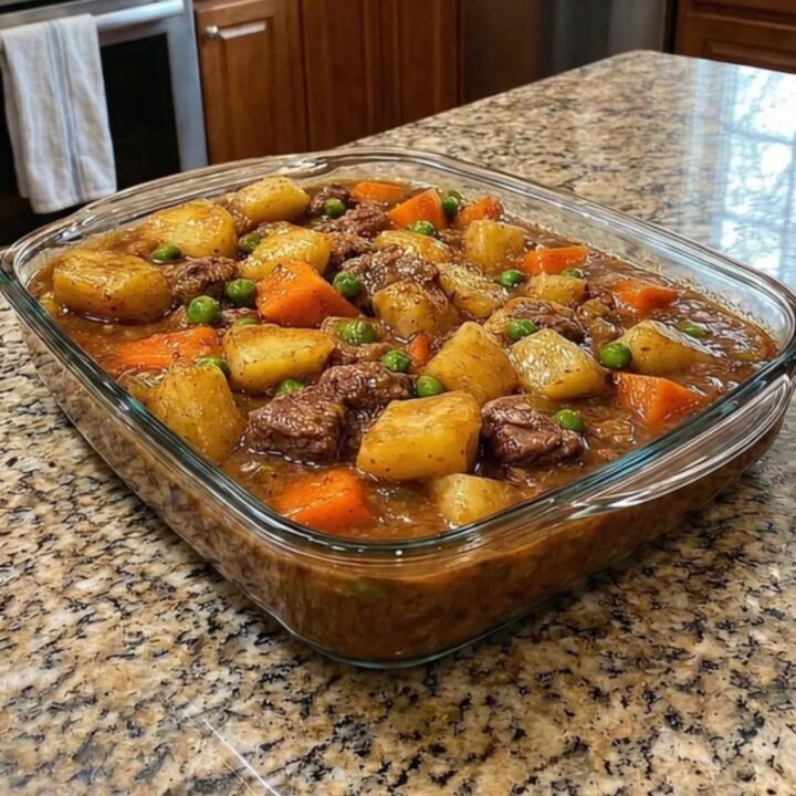 A steaming portion of beef stew casserole in a white bowl with chunks of beef and potatoes.