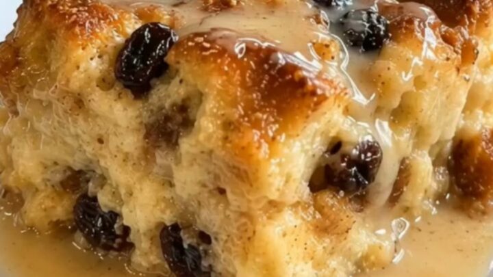 A warm square of New Orleans bread pudding drizzled with glossy bourbon sauce in a glass baking dish.