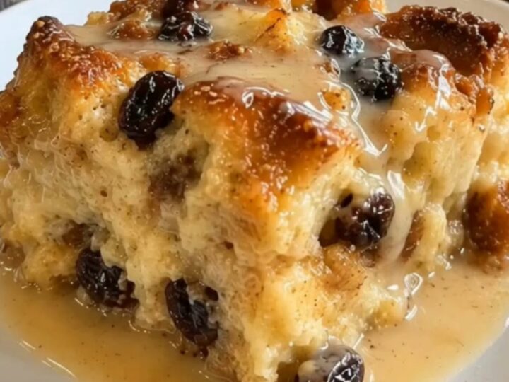 A warm square of New Orleans bread pudding drizzled with glossy bourbon sauce in a glass baking dish.