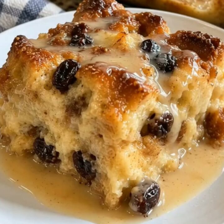 A warm square of New Orleans bread pudding drizzled with glossy bourbon sauce in a glass baking dish.