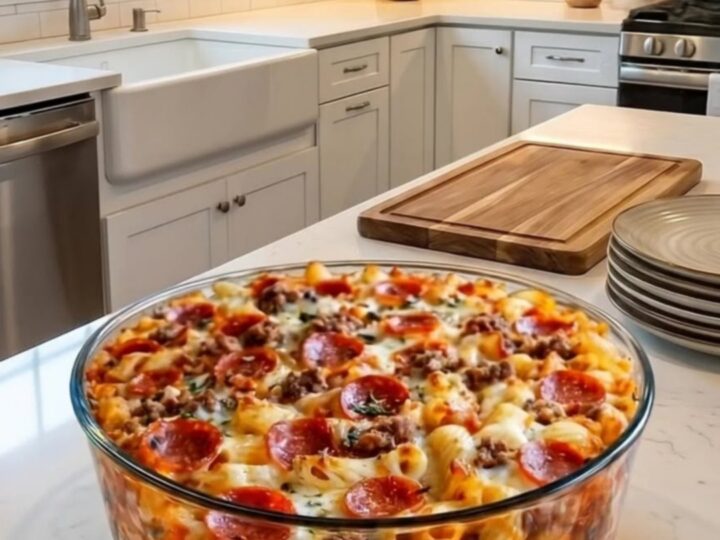 A deep glass baking dish filled with rigatoni pasta, pepperoni, and melted mozzarella cheese.